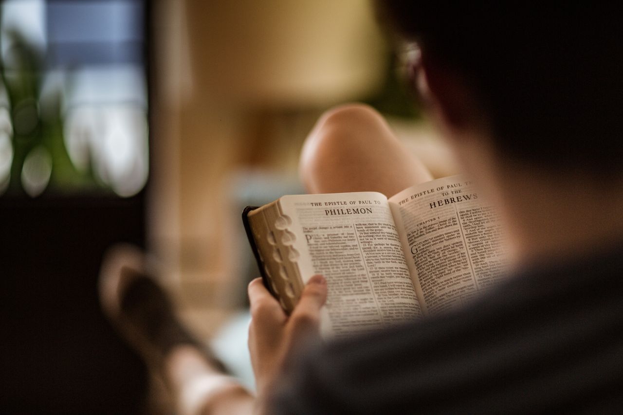 Ein Mann sitzt auf einer Couch und liest in der Bibel, sie ist beim Brief des Paulus an Philemon aufgeschlagen